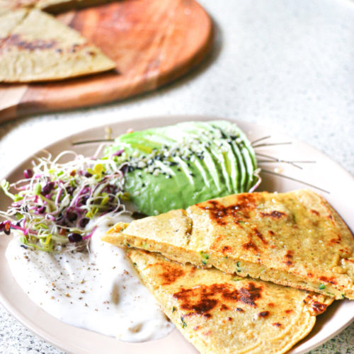 Chickpea flatbread on a plate with sliced avocado and mayonnaise