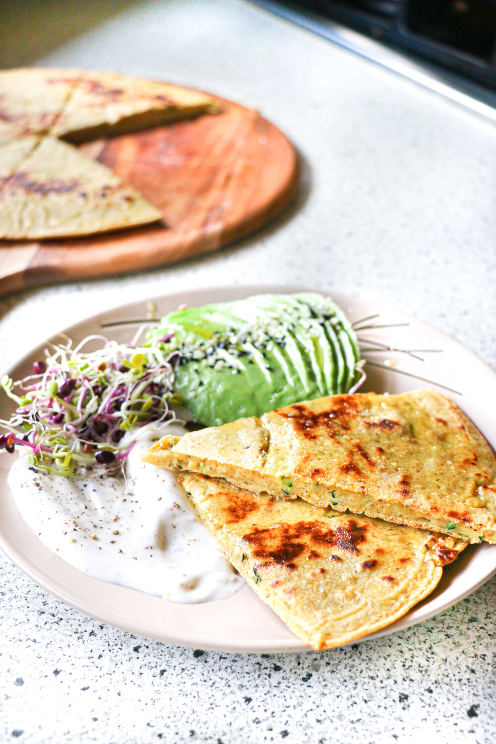 Chickpea flatbread on a plate with sliced avocado and mayonnaise